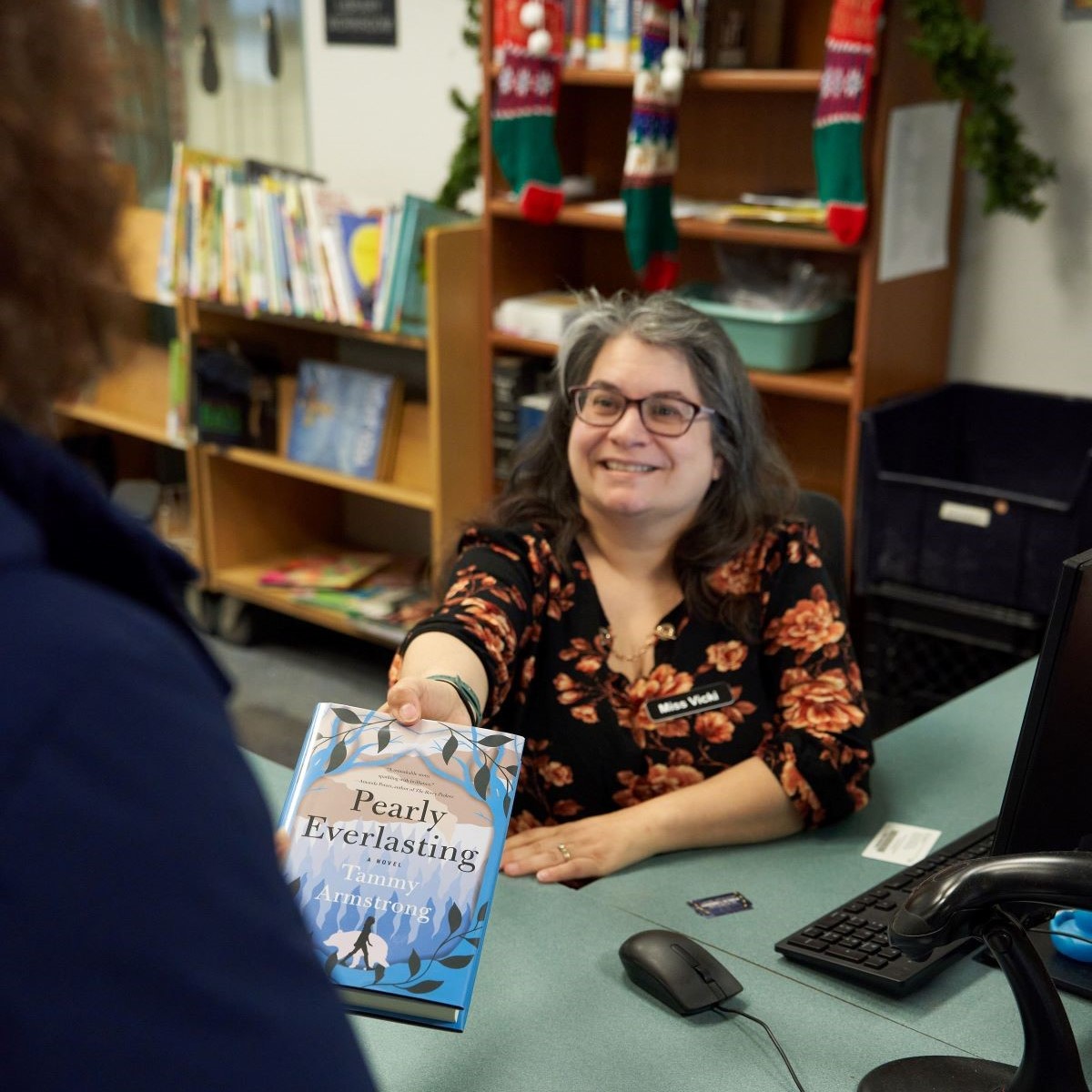 Library staff member behind desk handing a book to a person