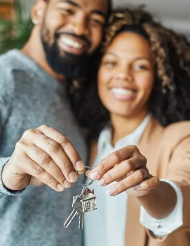 A man and woman holding a key to a house toward the camera