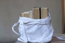 Grey background. White totebag sitting on table, open to show 4 books inside.